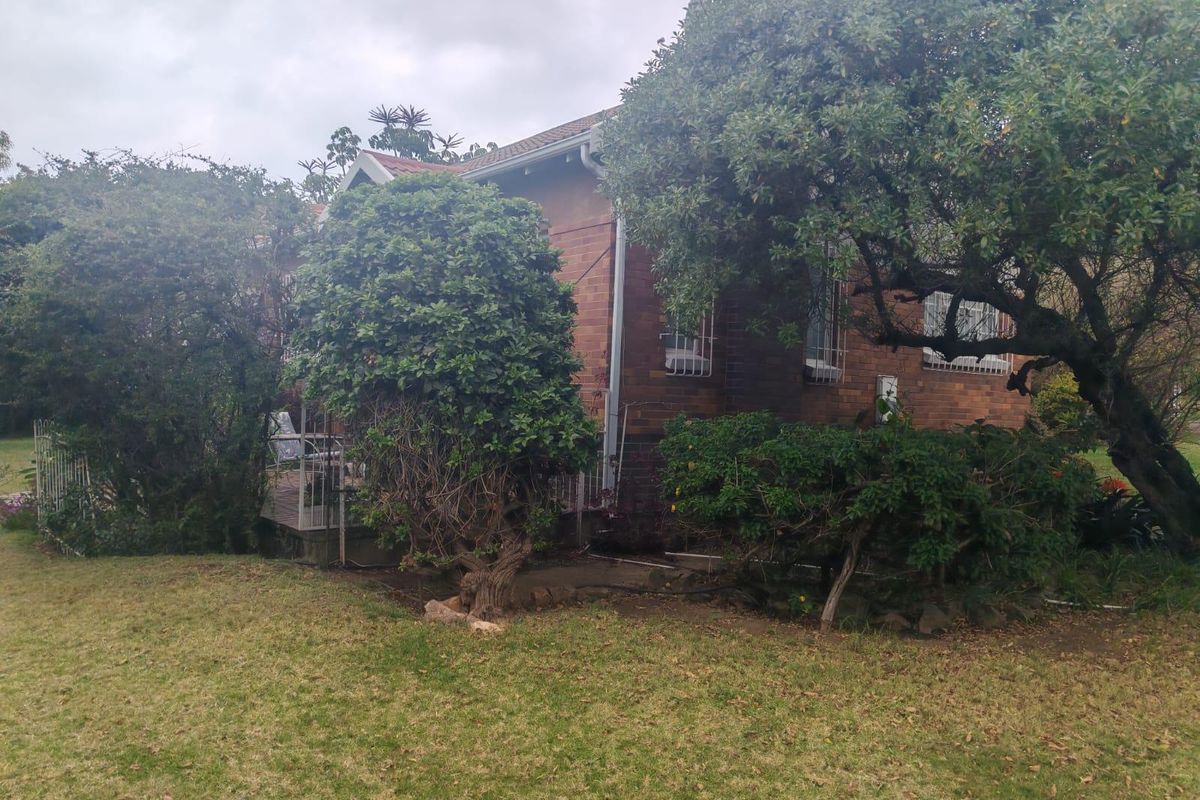 A view of the rear brick facade of the house, featuring established garden landscaping and security bars on the windows.