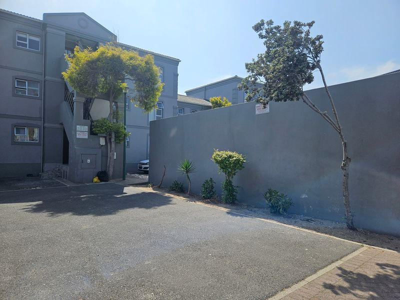 Exterior view of the apartment complex showing the building facade, staircase, and paved driveway area with a boundary wall.
