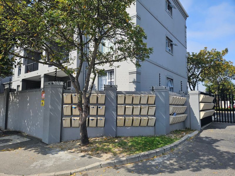 Exterior view of the apartment complex featuring a perimeter wall with integrated mailboxes, security electric fencing, and a gated entrance.