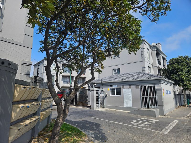Front entrance view of the apartment complex featuring a security gate, guard house, and wall-mounted post boxes.