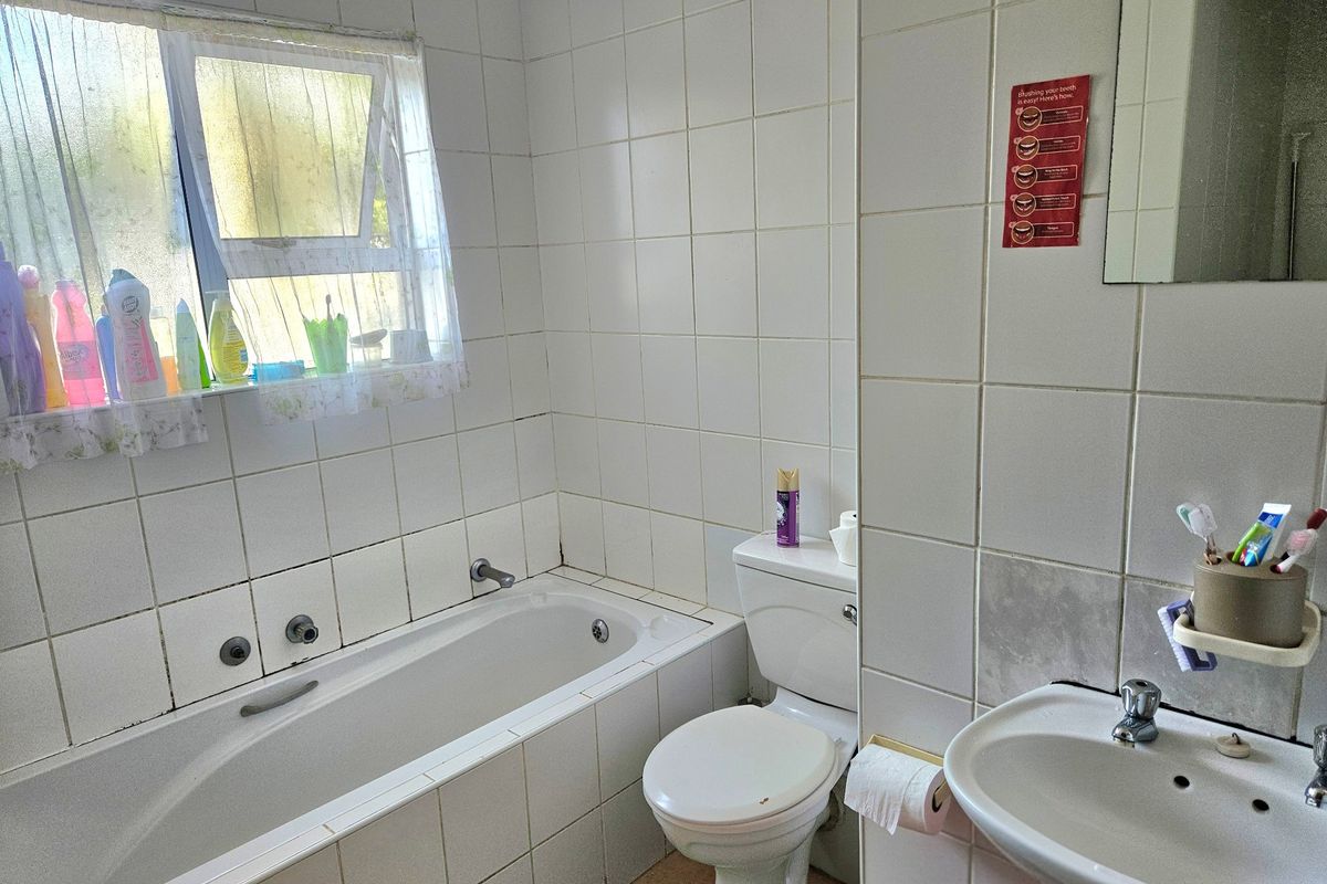 A functional bathroom featuring a built-in bathtub, pedestal sink, and toilet, finished with white ceramic wall tiles throughout.
