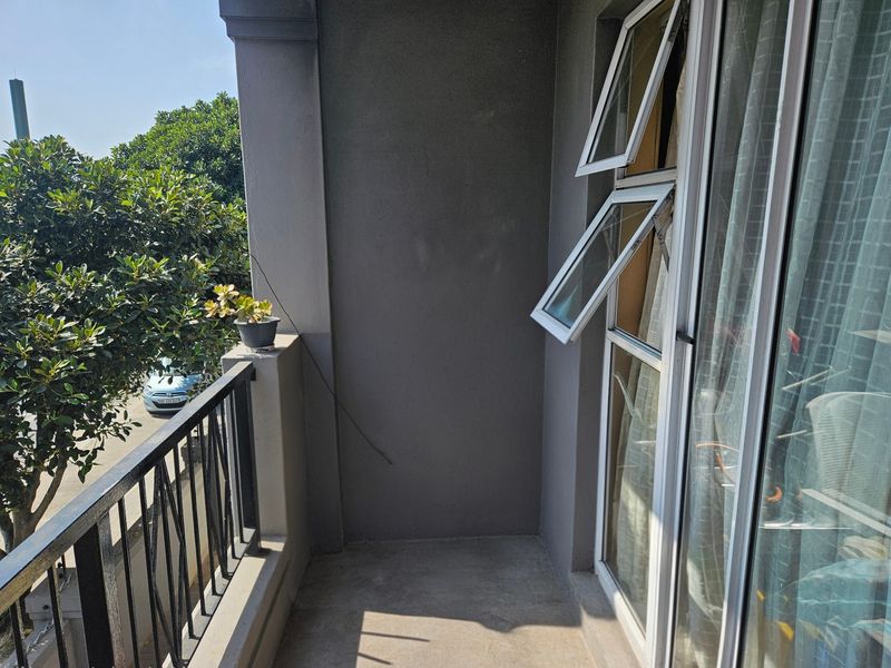 A private apartment balcony featuring a metal balustrade, concrete flooring, and aluminium window frames overlooking the street.