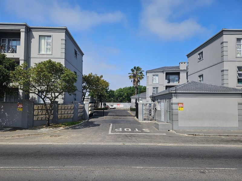 Front entrance view of the apartment complex featuring a secure gated access point, perimeter walls, and a dedicated guard house.