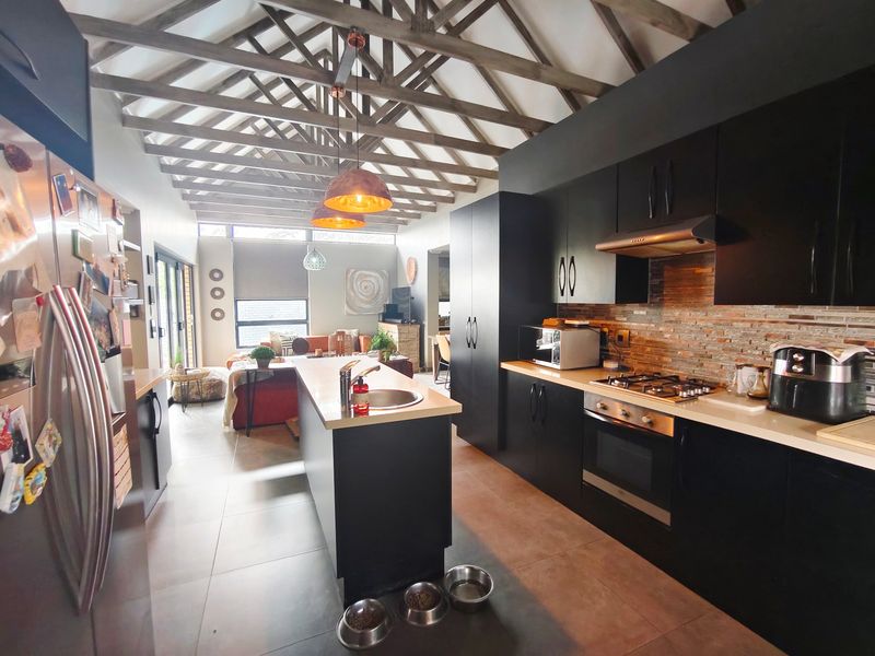 Spacious open-plan kitchen and living area featuring striking exposed timber roof trusses, modern black cabinetry, a central island, and high-quality stone tile flooring.