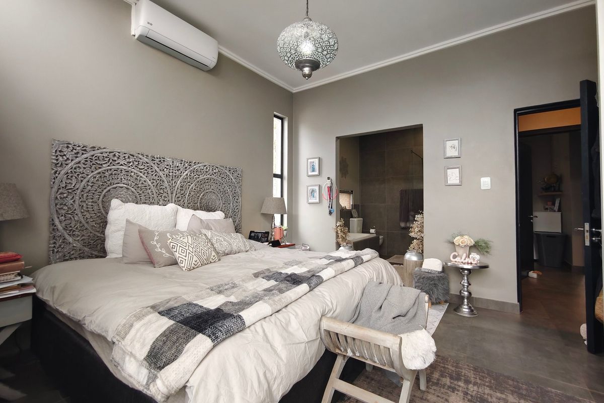 A well-maintained bedroom featuring neutral wall tones, tiled flooring, a split-system air conditioner, and direct access to an en-suite bathroom.