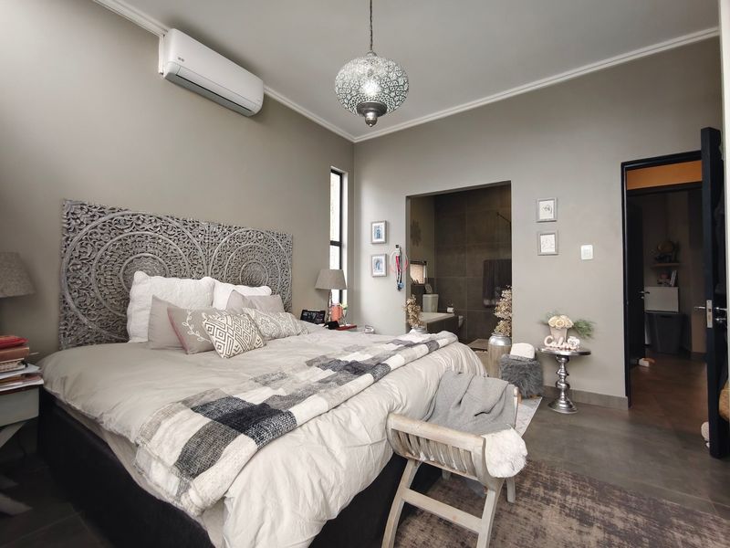 A well-maintained bedroom featuring neutral wall tones, tiled flooring, a split-system air conditioner, and direct access to an en-suite bathroom.
