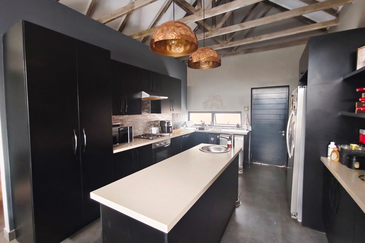 Modern kitchen featuring dark cabinetry, stone countertops, a central island, and striking exposed timber roof trusses, creating a contemporary and spacious culinary environment.