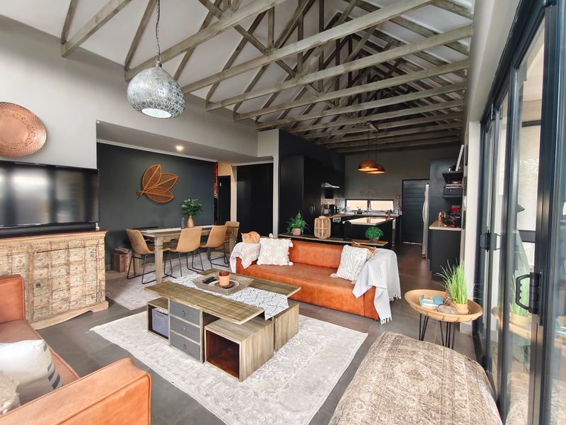 Spacious open-plan living and kitchen area featuring high vaulted ceilings with exposed timber trusses and large sliding doors leading to the outdoors.