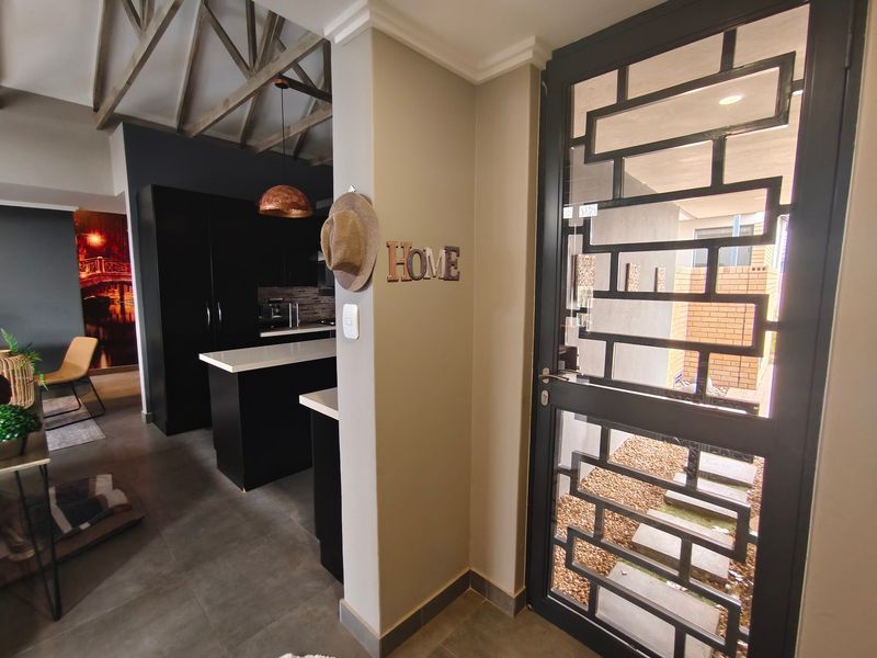 Entrance area featuring a modern security gate, tiled flooring, and an open-plan view into the kitchen with exposed timber roof trusses.