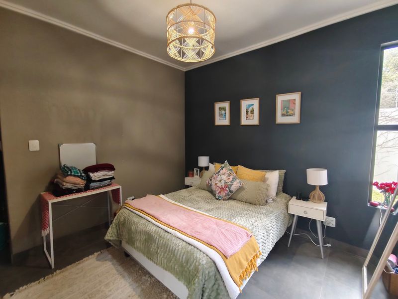 A well-lit bedroom featuring tiled flooring, a large window, and a modern accent wall, providing a comfortable and functional living space.