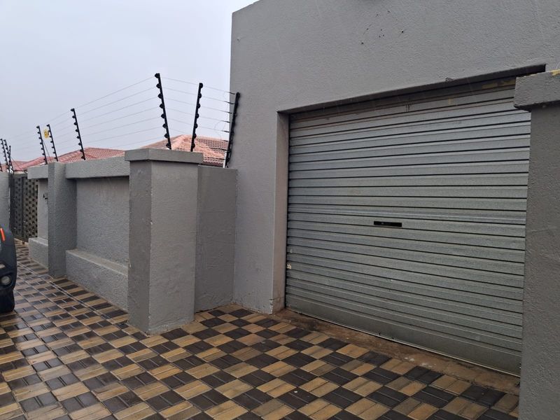 Exterior view of a garage featuring a secure roller shutter door, perimeter wall with electric fencing, and a paved driveway.