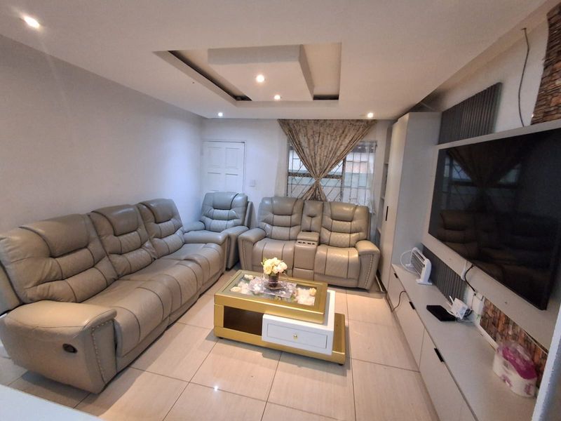 A well-maintained living room featuring tiled flooring, a modern recessed ceiling with downlights, and a built-in media unit.