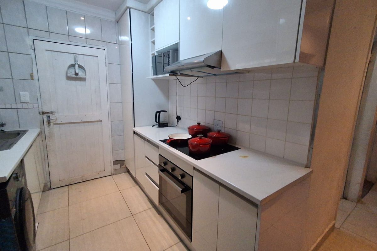 Compact kitchen featuring white high-gloss cabinetry, stone countertops, integrated oven, hob, and extractor fan with tiled backsplash and flooring.