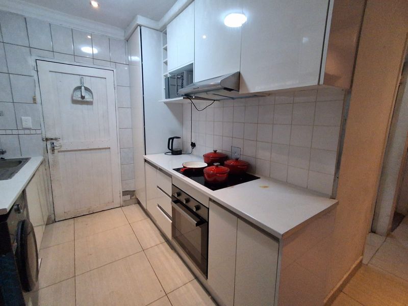 Compact kitchen featuring white high-gloss cabinetry, stone countertops, integrated oven, hob, and extractor fan with tiled backsplash and flooring.