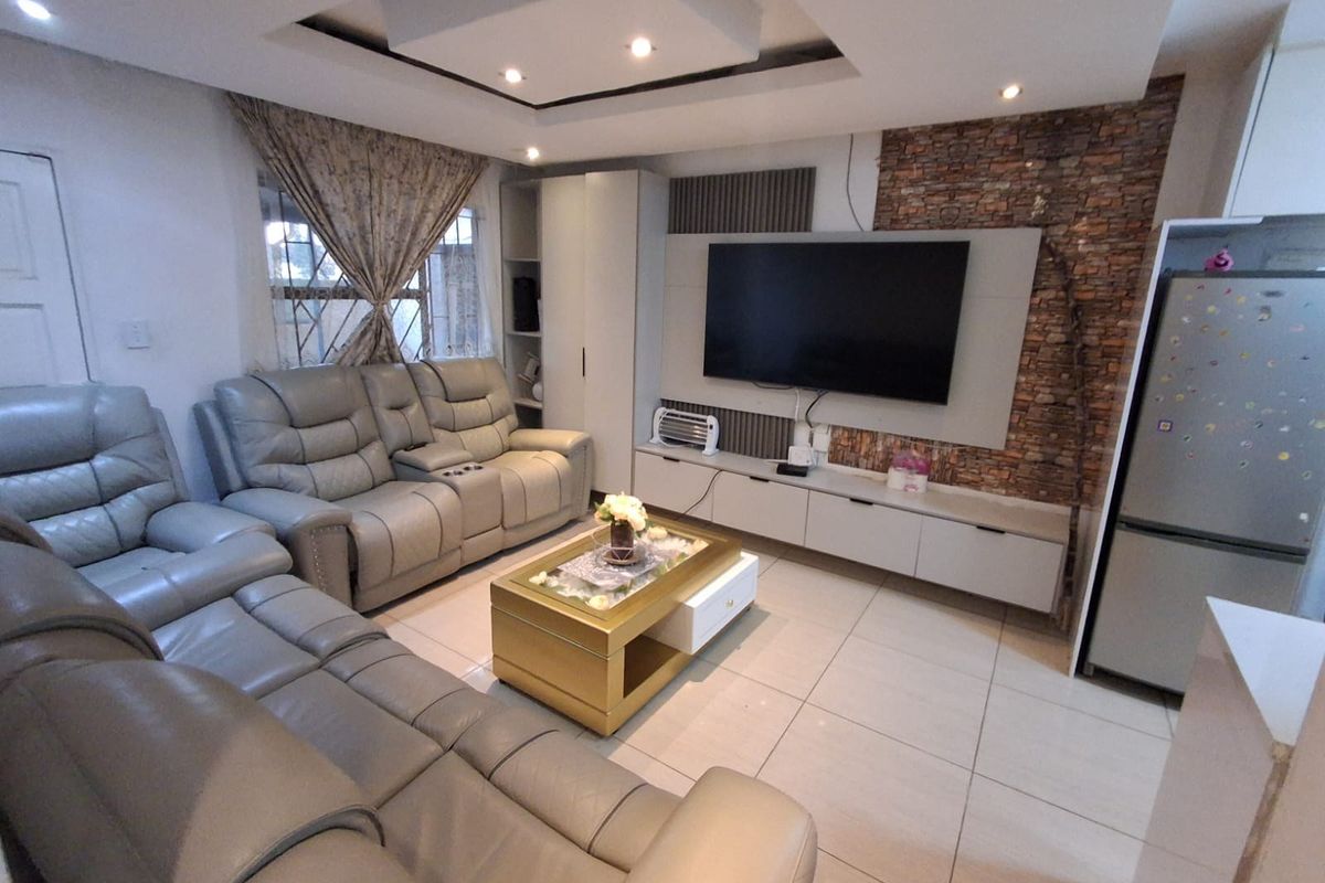 A modern living room featuring a stone veneer accent wall, built-in media cabinetry, recessed ceiling with downlights, and neutral tiled flooring.