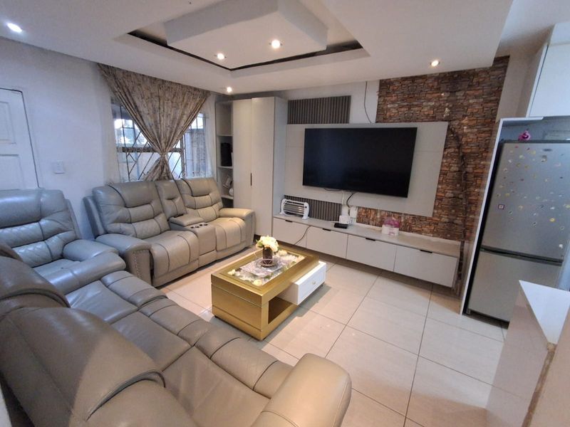 A modern living room featuring a stone veneer accent wall, built-in media cabinetry, recessed ceiling with downlights, and neutral tiled flooring.