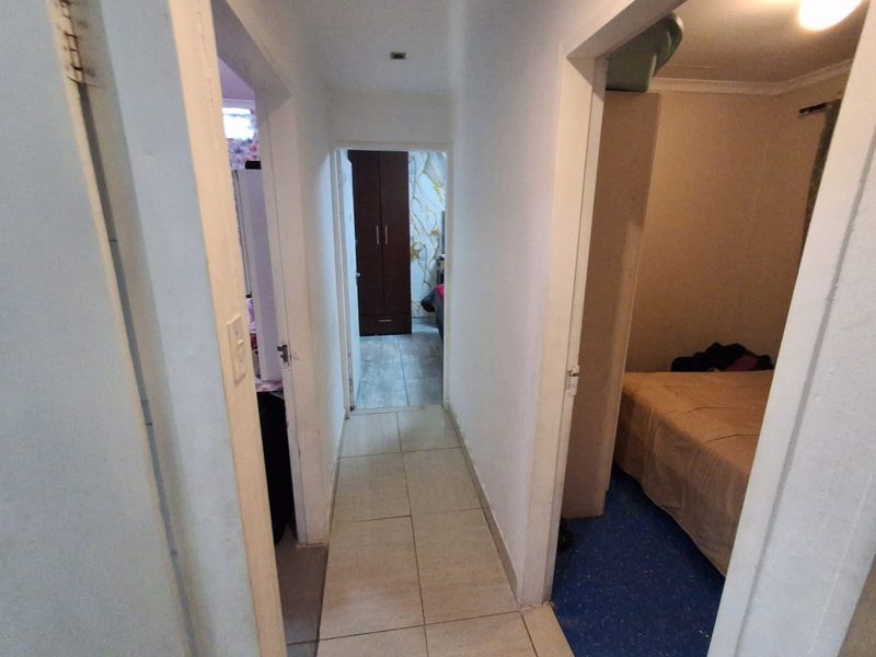 A narrow interior hallway with tiled flooring providing access to adjacent bedrooms and living areas.