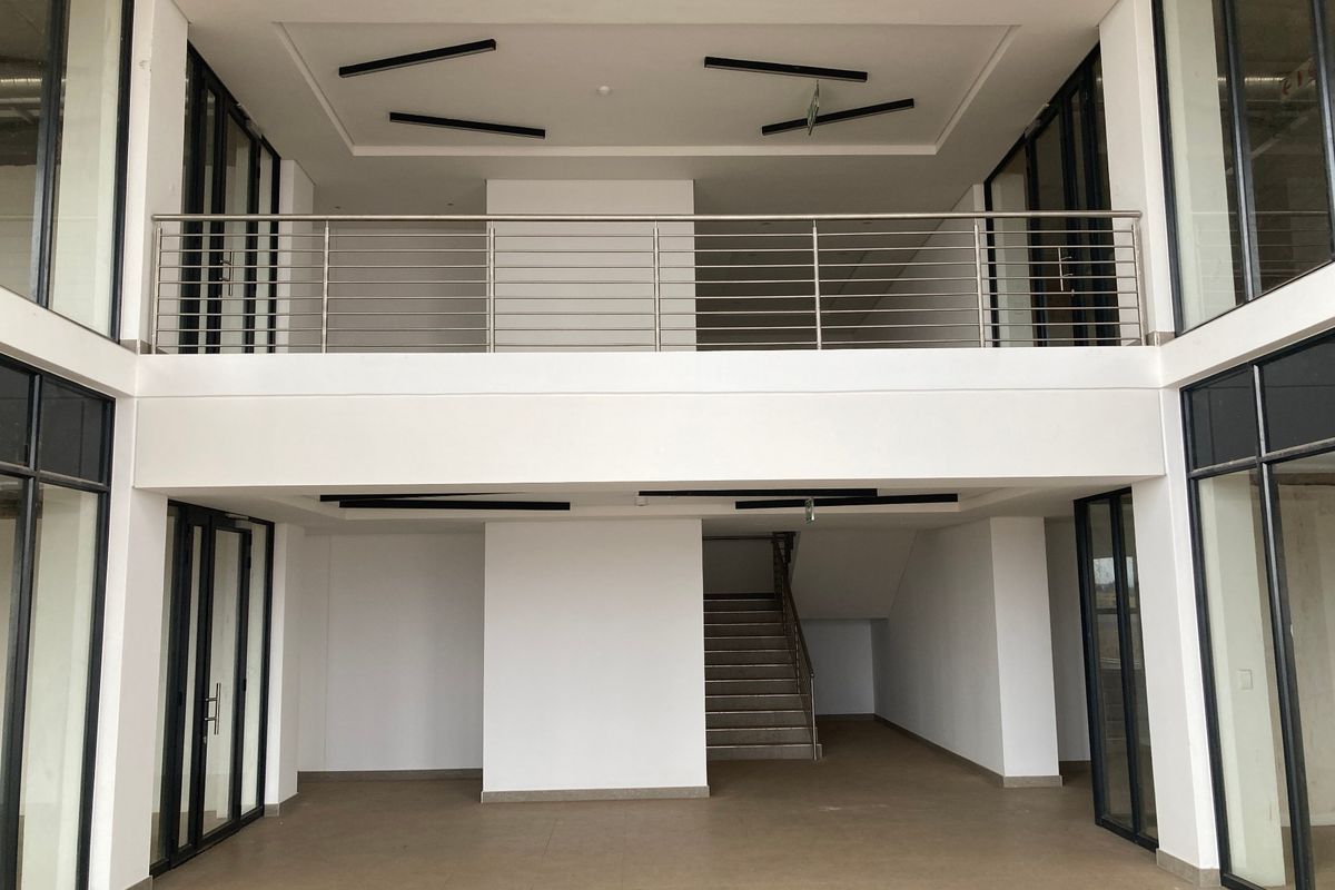 Spacious open-plan industrial office area featuring a mezzanine level, modern stainless steel balustrades, and extensive black-framed glass partitioning for natural light.