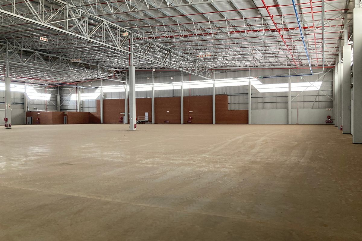 Spacious industrial warehouse featuring high ceilings with exposed steel trusses, fire sprinkler systems, concrete flooring, and brick and metal wall cladding.