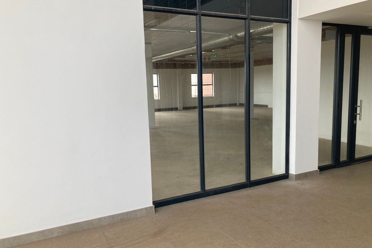 An open-plan industrial office space featuring exposed ductwork, large black-framed glass partitions, and neutral tiled flooring, offering a clean and modern professional environment.