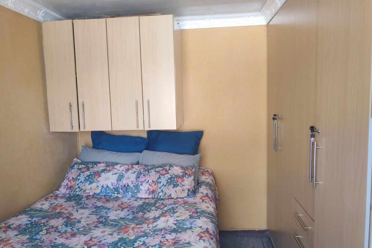 A compact bedroom featuring built-in wooden cabinetry and decorative ceiling cornicing, providing essential storage space.