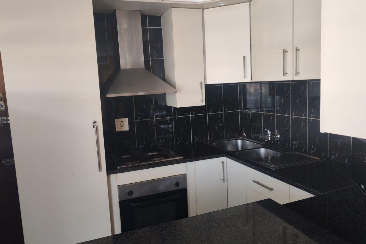 Compact kitchen featuring white cabinetry, black granite countertops, stainless steel appliances, and a contrasting black tiled backsplash.
