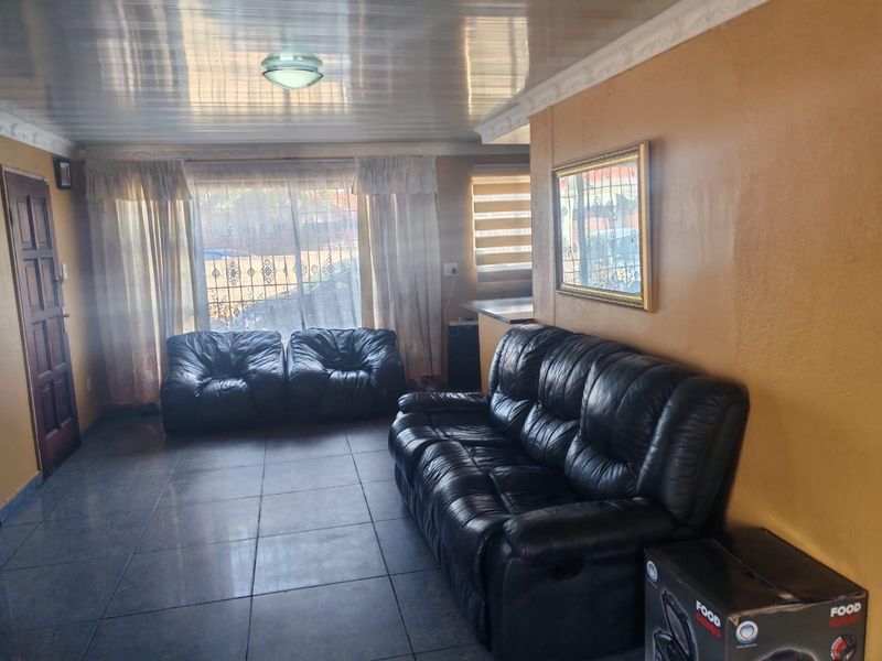 A living room featuring tiled flooring, decorative ceiling cornicing, and natural light through a window with security bars.