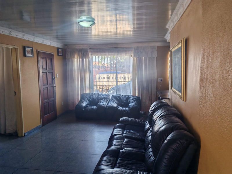 A living room featuring tiled flooring, decorative ceiling moulding, and a security gate over the window.