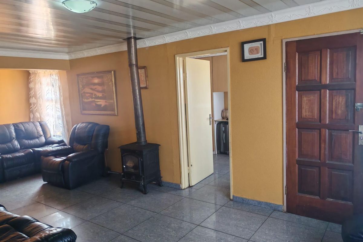 Living room featuring a wood-burning stove, tiled flooring, and a panelled ceiling, with direct access to an adjacent room.
