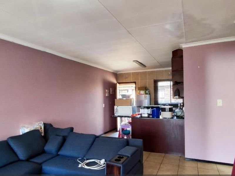 Open plan living and kitchen area featuring tiled flooring and a breakfast bar, requiring cosmetic updates and ceiling repairs.