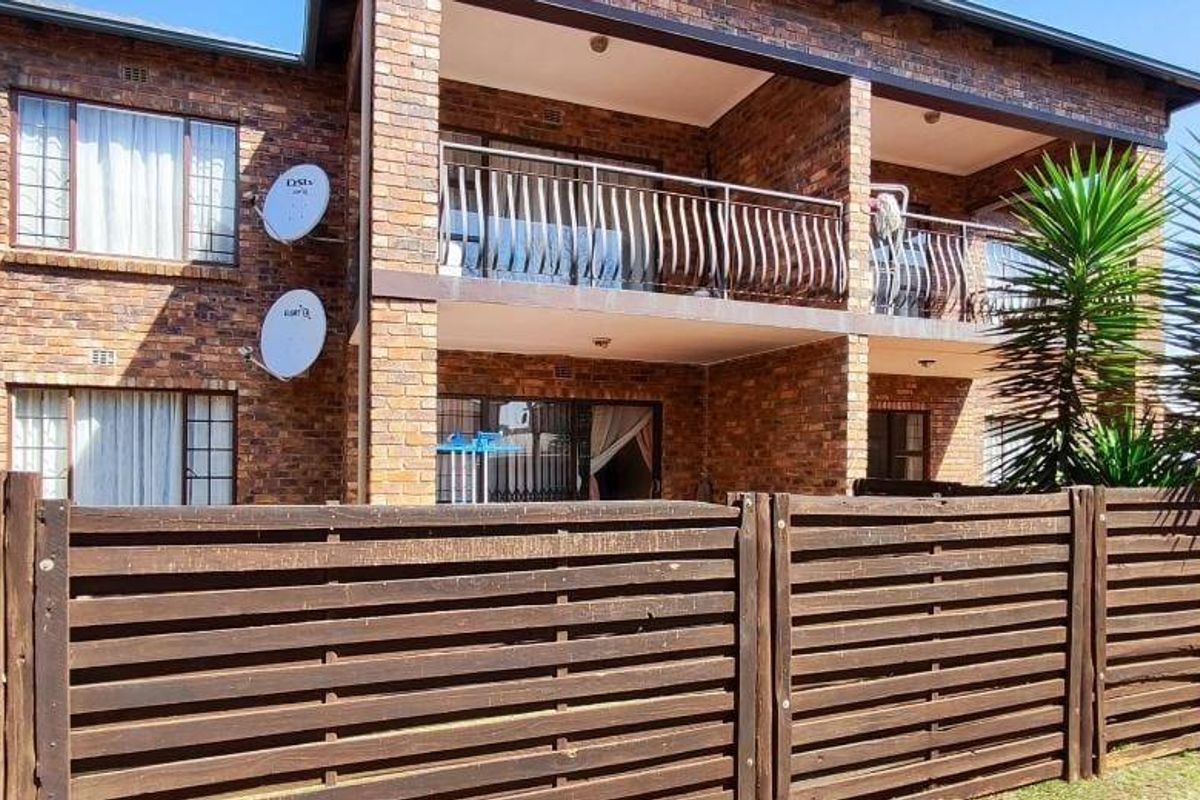 Rear view of a double-story face brick apartment building featuring balconies with metal balustrades and a timber slat boundary fence.