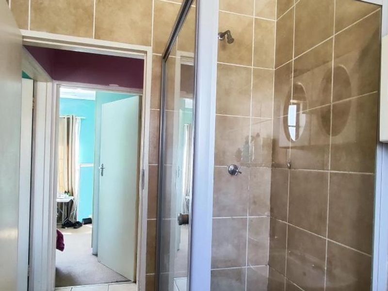 A functional bathroom featuring a tiled shower enclosure and a built-in wall cabinet, with direct access to the hallway.