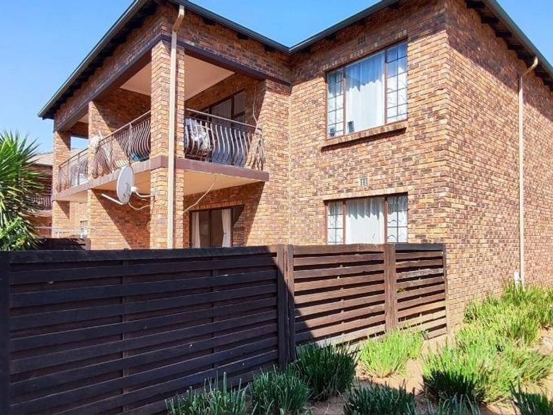 Rear view of a face brick apartment building featuring a private balcony with wrought iron balustrade and enclosed timber fencing.