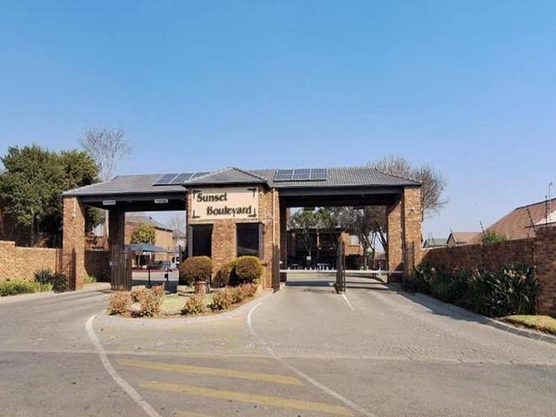 The main entrance and security gatehouse of the Sunset Boulevard apartment complex, featuring brick construction and paved access.
