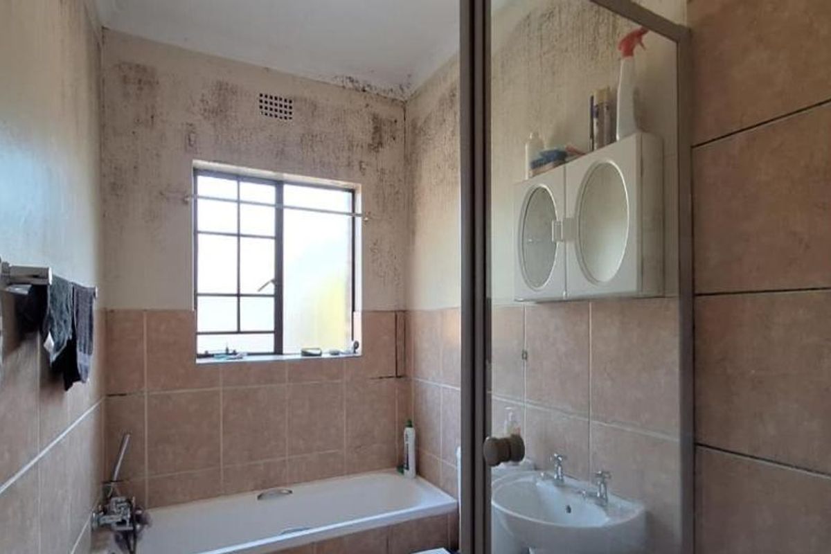 A bathroom featuring a bathtub and pedestal sink, currently requiring significant maintenance and repair due to visible wall surface damage and staining.