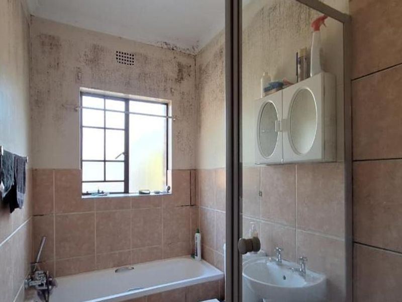 A bathroom featuring a bathtub and pedestal sink, currently requiring significant maintenance and repair due to visible wall surface damage and staining.