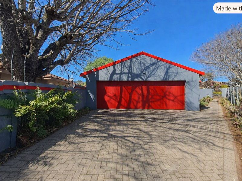 A detached double garage featuring vibrant red doors and matching trim, set against a paved driveway and secure perimeter wall with electric fencing.