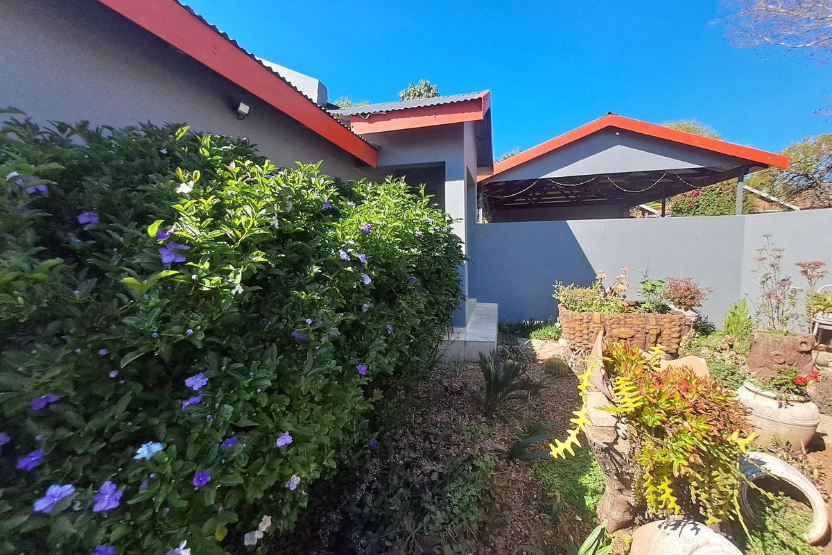 Rear exterior view of the property featuring a carport, landscaped garden area, and well-maintained boundary walls with a corrugated metal roof.