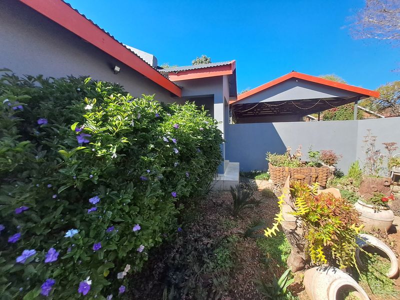 Rear exterior view of the property featuring a carport, landscaped garden area, and well-maintained boundary walls with a corrugated metal roof.