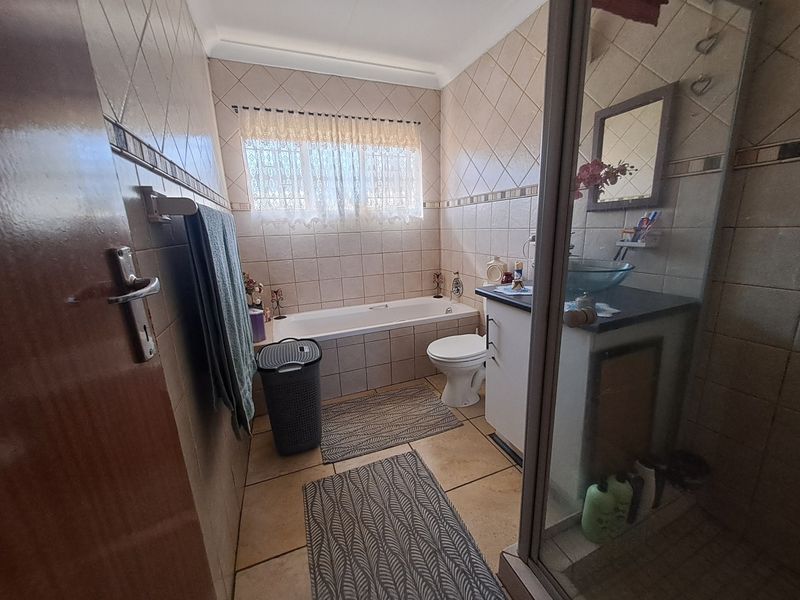 A functional bathroom featuring a built-in bathtub, a separate shower enclosure, and a vanity unit with a vessel sink, finished with neutral ceramic tiling.
