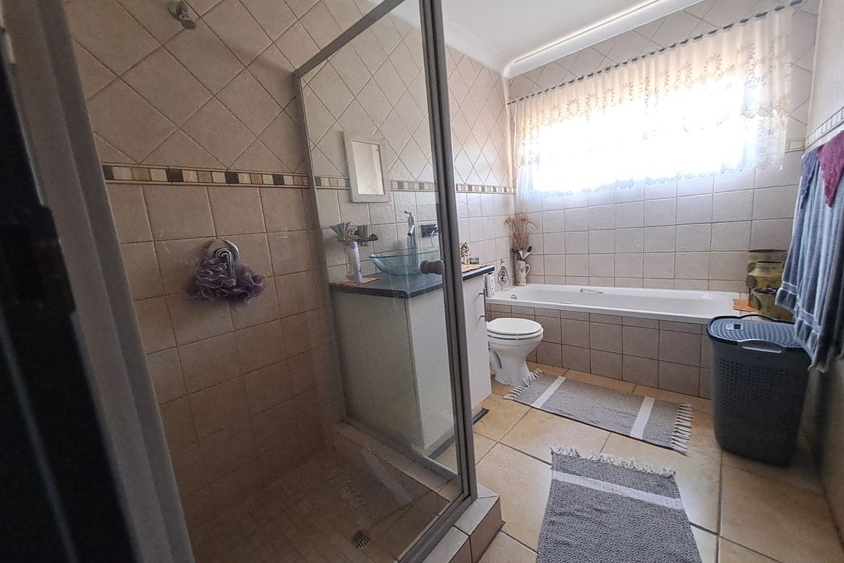 A functional bathroom featuring a glass-enclosed shower, a bathtub, a vanity with a vessel sink, and neutral wall and floor tiling.