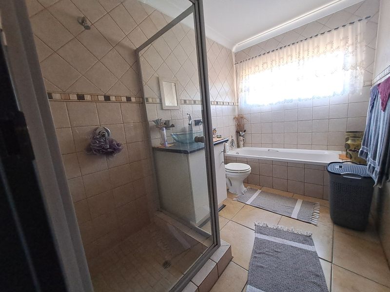 A functional bathroom featuring a glass-enclosed shower, a bathtub, a vanity with a vessel sink, and neutral wall and floor tiling.