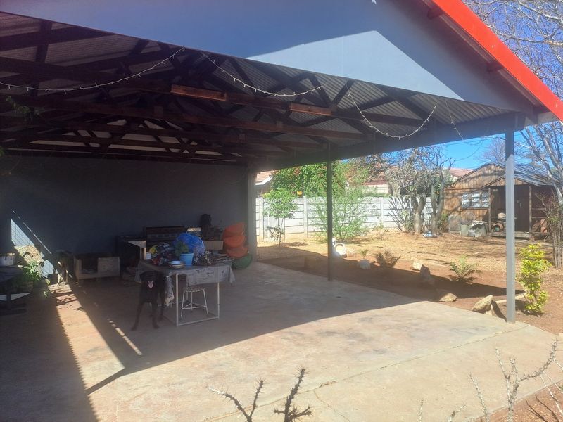 A spacious covered outdoor patio featuring exposed timber roof trusses, concrete flooring, and steel supports, overlooking a large rear garden area.