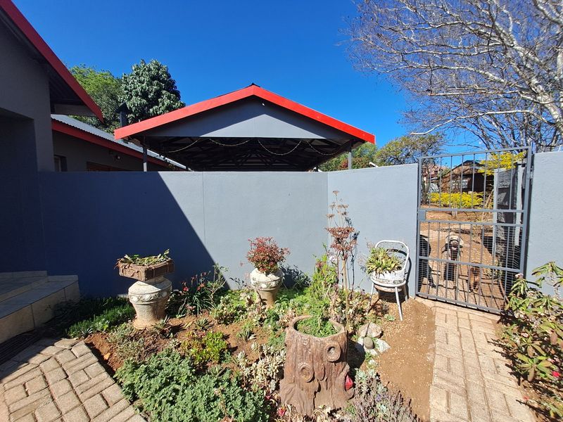 Front exterior view featuring a paved walkway, boundary wall, metal gate, and a covered carport structure.