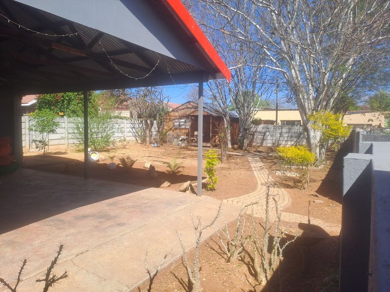 A covered patio area overlooking a backyard with a paved walkway, precast boundary walls, and established trees.