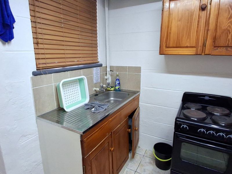 Compact kitchen featuring wooden cabinetry, a stainless steel sink, tiled backsplash, and a freestanding electric stove.