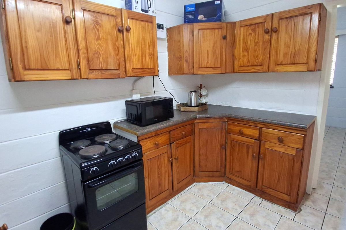A functional kitchen featuring traditional wooden cabinetry, laminate countertops, and a freestanding electric stove with tiled flooring.