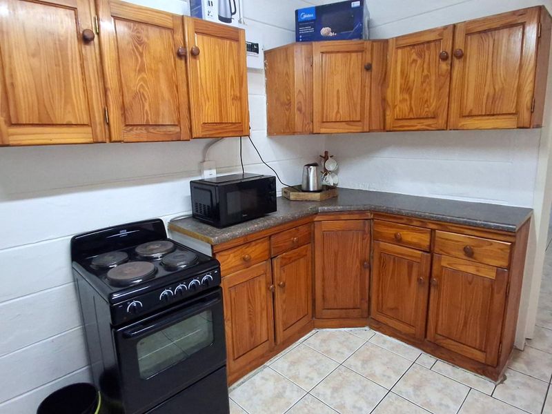 A functional kitchen featuring traditional wooden cabinetry, laminate countertops, and a freestanding electric stove with tiled flooring.