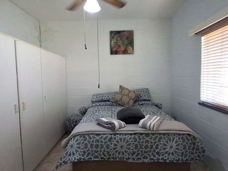 A compact bedroom featuring built-in wardrobes, a ceiling fan, and venetian blinds, with tiled flooring throughout.