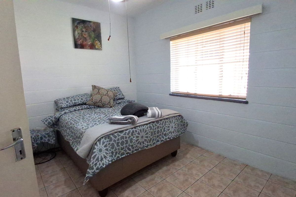 A functional bedroom featuring tiled flooring, a window with venetian blinds, and a ceiling light fixture.